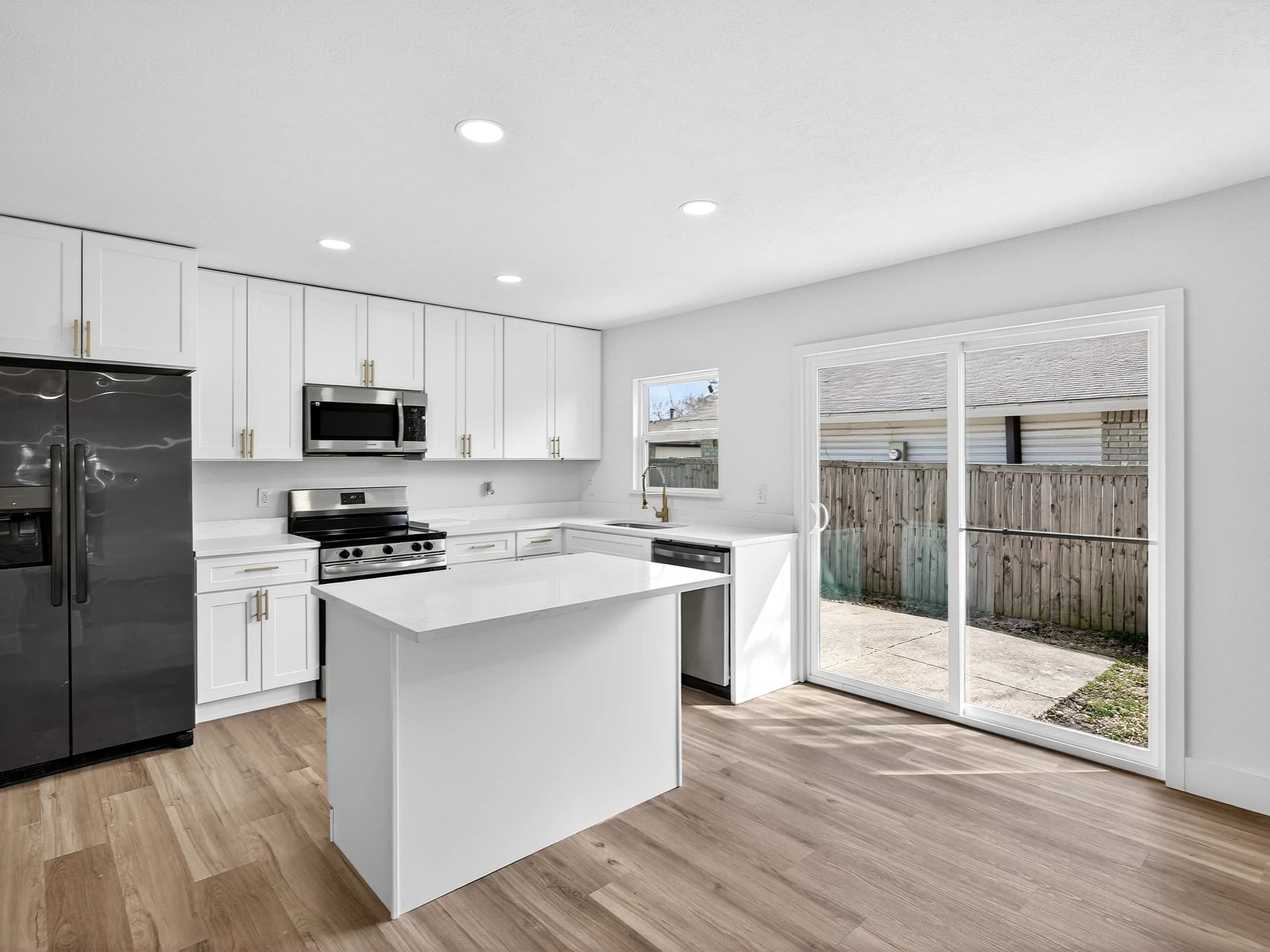 White island kitchen with stainless range, dark refrigerator, warm-toned handles and a sliding glass door