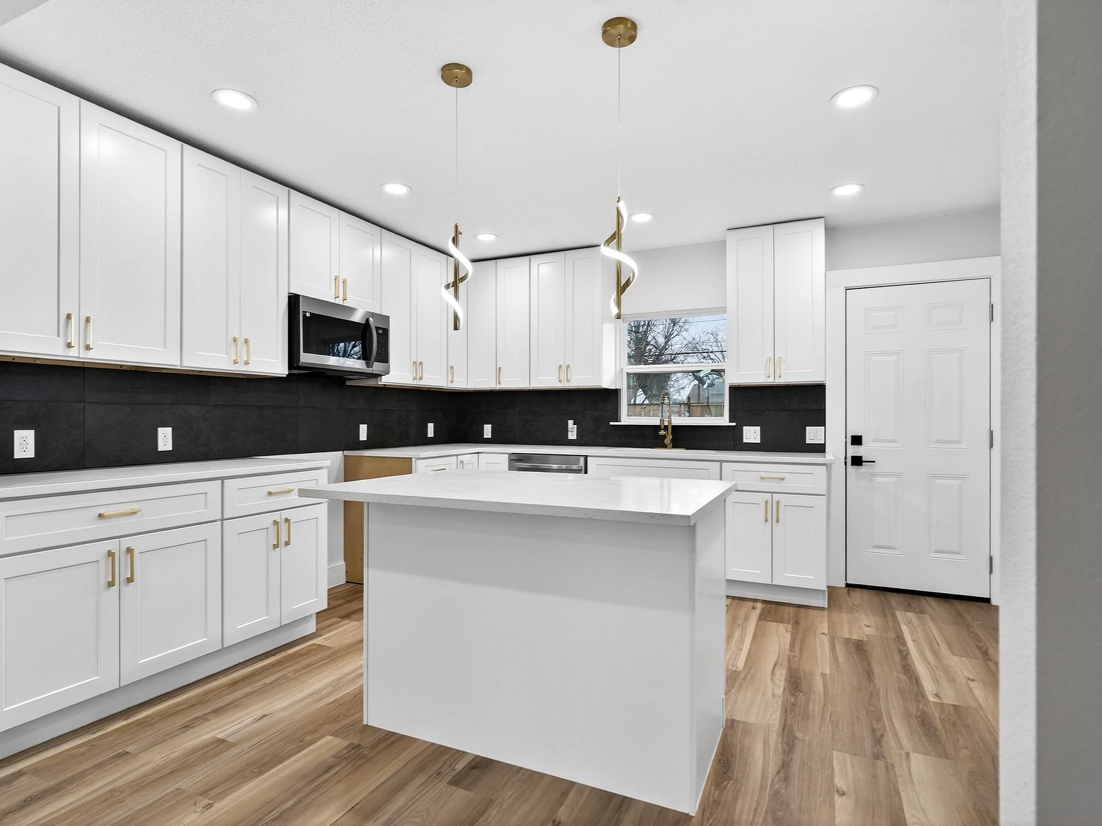 White island kitchen with dark backsplash, brass-toned hardware and two sculptural pendant lights