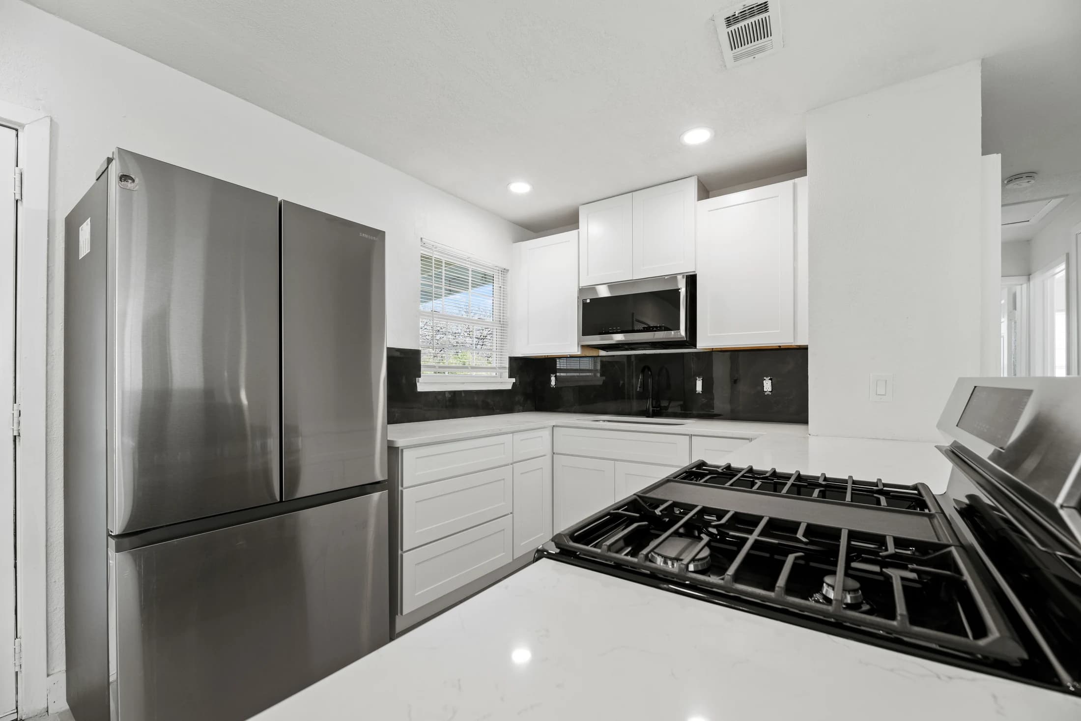Remodeled kitchen with white cabinets, dark backsplash, stainless refrigerator and gas range