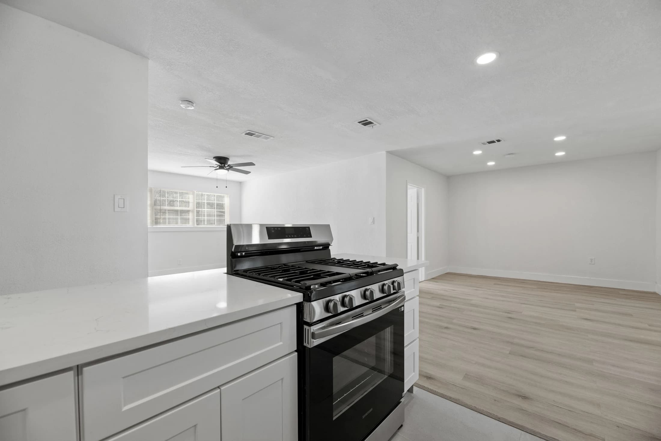 View across a white kitchen peninsula and gas range toward the bright adjoining living room