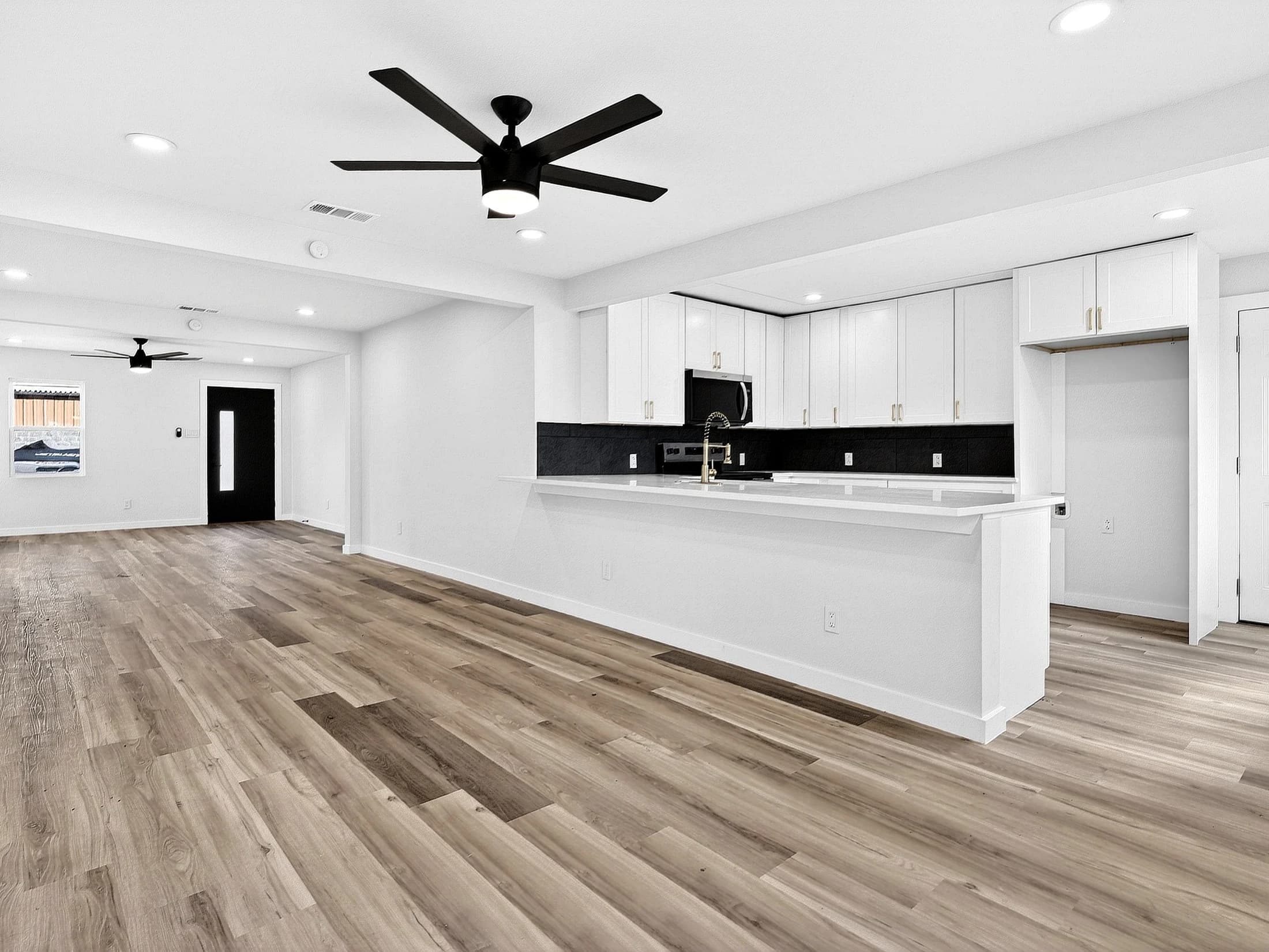 Continuous wood-look flooring across an open living area toward a white kitchen peninsula and dark front door