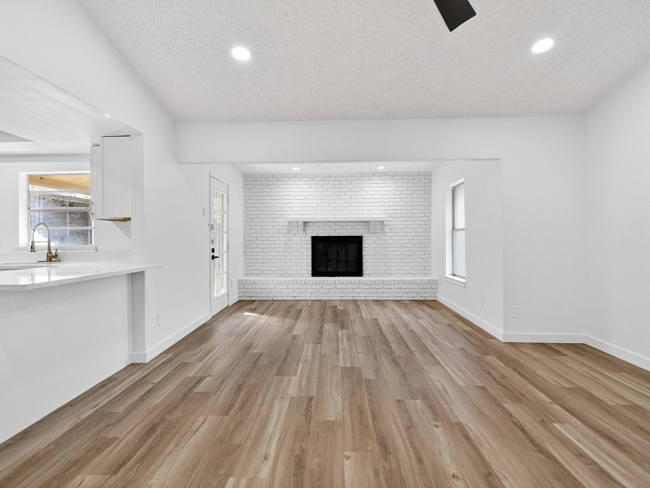 Wood-look plank flooring leading past a kitchen peninsula toward a white brick fireplace and glass door